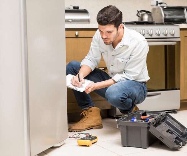 Portrait of a handsome male technician doing a work report on a broken fridge in a home kitchen